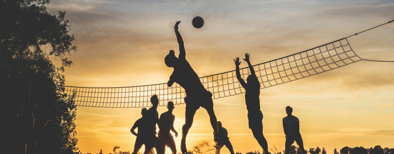 A silhouette of people playing volleyball at the beach at dusk