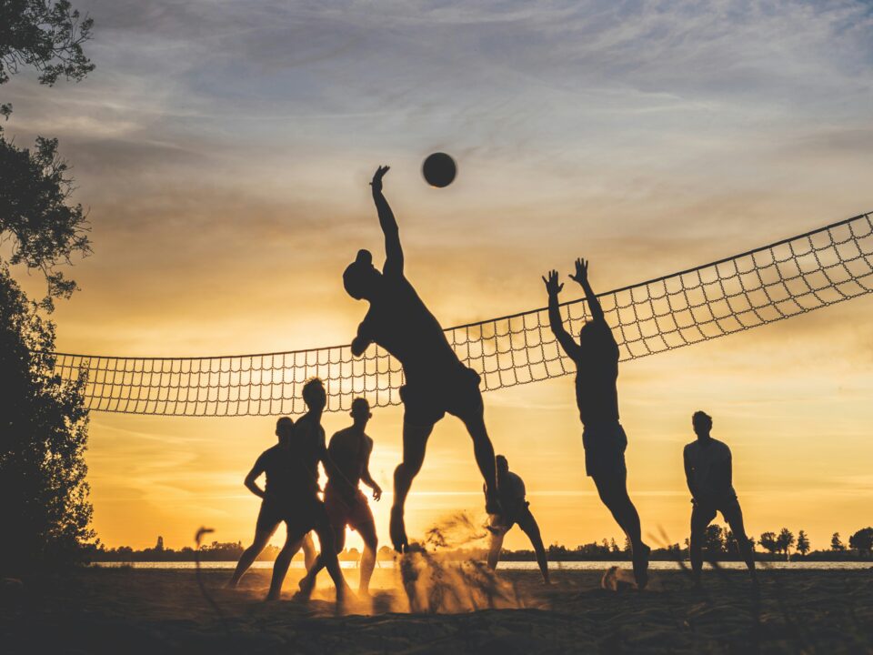 A silhouette of people playing volleyball at the beach at dusk